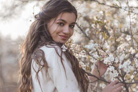 Pretty smiling teen girl are posing in garden near blossom cherry tree with white flowers.の写真素材