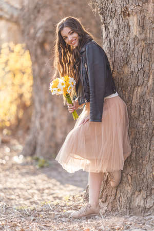 Portrait of smiling teenager girl are wearing casual clothes holding bouquet of narcissus flowers in park over sunset lights. Spring timeの写真素材