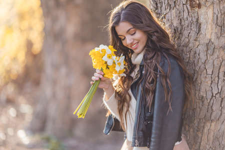 Portrait of smiling teenager girl are holding bouquet of narcissus flowers in park over sunset lights. Spring timeの写真素材