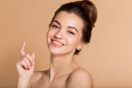 Happy smiling girl with perfect skin with moisturizing face cream on a cheek. Skin care and health concept.の写真素材