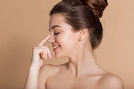 Happy smiling girl with perfect skin with moisturizing face cream on a cheek. Skin care and health concept.の写真素材