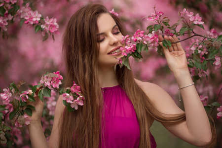 Portrait of young beautiful girl in blooming apple garden with pink flowers, spring time