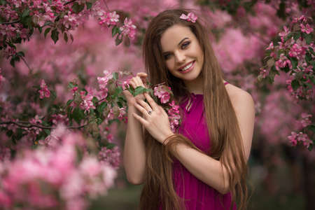 Portrait of young beautiful girl in blooming apple garden with pink flowers, spring timeの写真素材