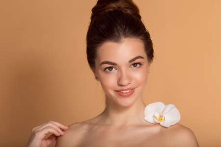 Closeup portrait of young beautiful girl with flawless skin with white orchid flower on her shoulder. Skin care, beauty and cosmetics concept.の写真素材