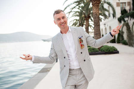 Stylish businessman is wearing white fashion costume stands on the background of the bay with luxury...