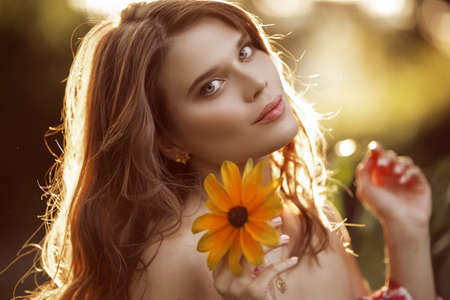 Outdoor fashion photo of beautiful young woman with yellow flowerの写真素材