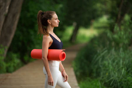 Pretty sportive girl with yoga mat outdoors in green park, summer timeの写真素材