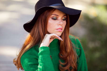 Sunshine young teen girl with red curly hair is wearing green sweater and hat in autumn park.の写真素材