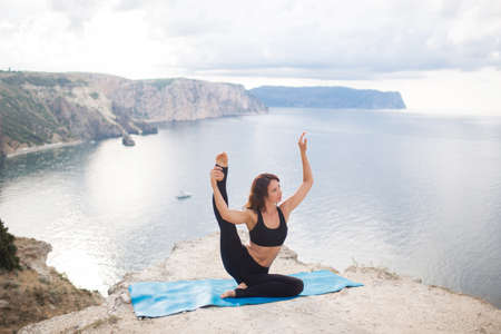 Beautiful slim woman practices yoga and pilates on the cliff of mountain with the sea view. Sportive and heathy lifestyle concept.の写真素材