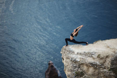 Beautiful slim woman practices yoga and pilates on the cliff of mountain with the sea view. Sportive and heathy lifestyle concept.の写真素材