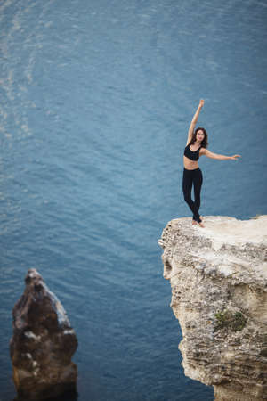 Beautiful slim woman practices yoga and pilates on the cliff of mountain with the sea view. Sportive and heathy lifestyle concept.の写真素材