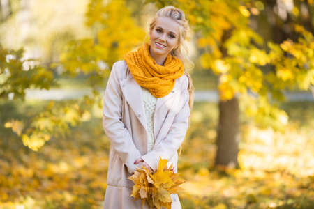 Pretty blonde teen girl is walking in autumn park with yellow leavesの写真素材