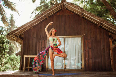 Yoga asana by young beautiful woman near wooden house in the tropical paradise with palms and banana trees on Zanzibar islandの写真素材