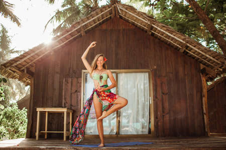 Yoga asana by young beautiful woman near wooden house in the tropical paradise with palms and banana trees on Zanzibar islandの写真素材