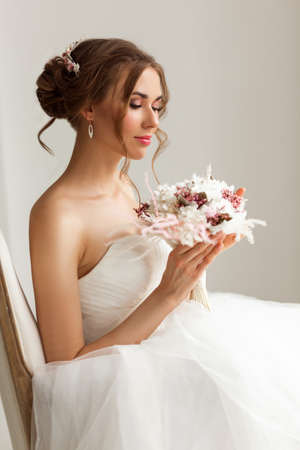 Close up portrait of young bride in a beautiful dress holding a bouquet of flowers in bright white studio. Wedding concept.の写真素材