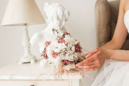 Young bride is wearing beautiful dress holding a bouquet of flowers in bright white studio. Wedding concept.の写真素材