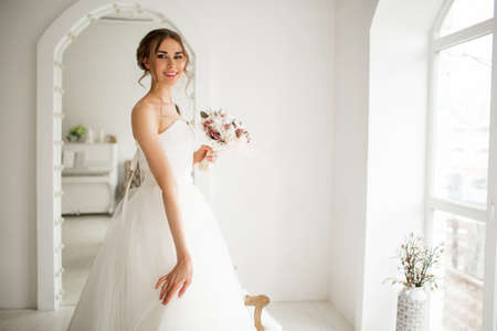 Young bride in a luxury dress holding a bouquet of flowers in bright white studio. Wedding fashion concept.の写真素材