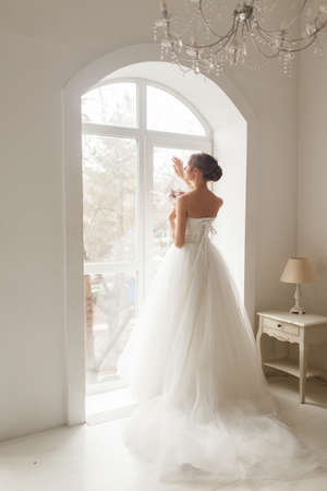 Young bride is wearing beautiful dress holding a bouquet of flowers in bright white studio. Wedding concept.の写真素材