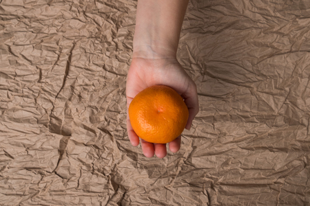 Mandarin in a female hand. Studio image of a tangerine in hand on the background of crumpled paper.の写真素材