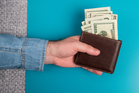 Male wallet with banknotes. Studio image. Men's hands hold a leather wallet with dollar bills.