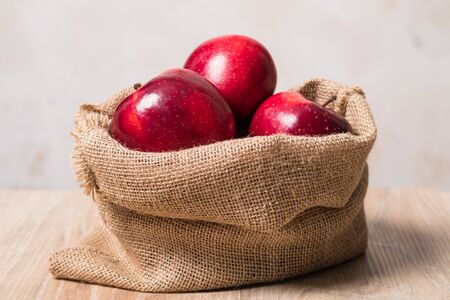 Bag with apples. Studio image. Red apples in a burlap bag on a wooden background. Fabric bag full of apples.の写真素材