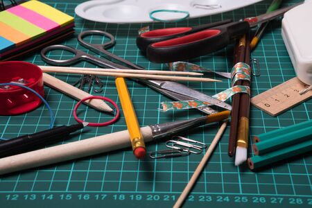 Stationery set studio image. Office, school supplies. Scissors, brushes, paper clips, pencils on a cutting mat.の写真素材
