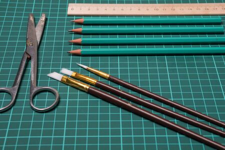 Stationery set studio image. Office, school supplies. Scissors, brushes, paper clips, pencils on a cutting mat.の写真素材