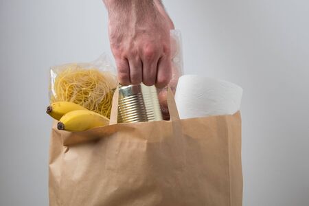 Volunteer with donation box with foodstuffs. Male hands hold a set of food products in a paper bag.の写真素材