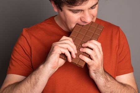Man eats a bar of chocolate. Caucasian man bites chocolate.の写真素材