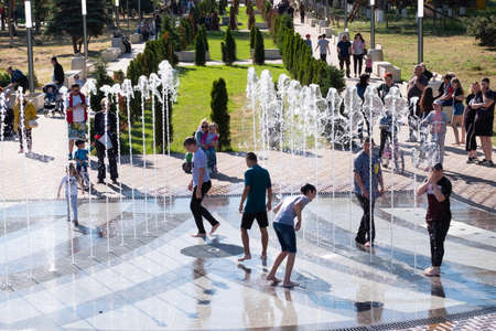 Kerch/Russia - May 31, 2020: Happy children laugh and splash in fountain in the summer park. People walk in the summer park.のeditorial素材