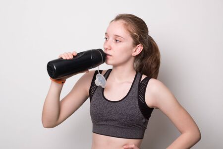 Young beautiful sporty girl doing sport wearing sportswear. Cute girl drinks water from a bottle.