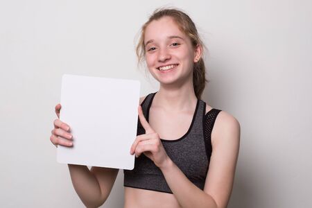 Positive girl holds a blank poster for text. Teen girl with a smile holds a white sheet for text.