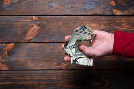 Crumpled dollars in a man's hand. Male hand holds crumpled bills on a wooden background.