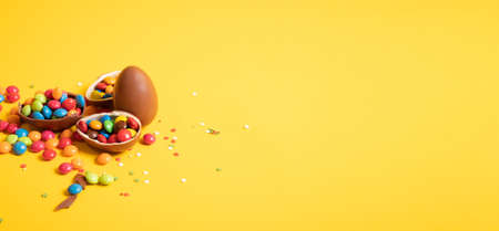 Banner. Chocolate Easter eggs with colored candies on a yellow background.