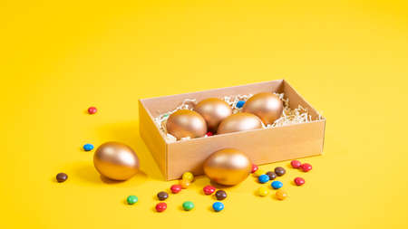 Golden Easter eggs in a gift box on a yellow background.