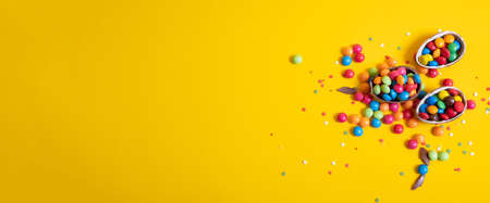 Banner. Chocolate Easter eggs with colored candies on a yellow background.