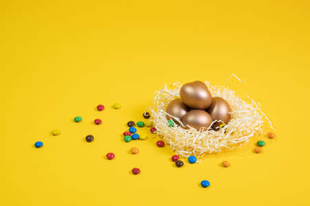 Easter background with colorful eggs in nest on a yellow background. Top view with copy space....