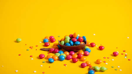 Banner. Chocolate Easter eggs with colored candies on a yellow background.の写真素材