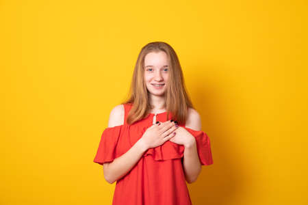 Cute blond beautiful girl feels thankful, presses palms to chest, looks with gratitude, heart...