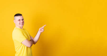 Banner copy spase. Portrait of a smiling man pointing finger away of  yellow background.の写真素材