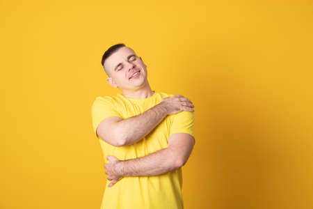 Young handsome man over yellow background Hugging oneself happy and positive, smiling confident. Self love and self care.の写真素材