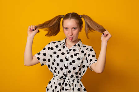 Funny teenage girl with a two-ponytail hairstyle smiles with braces grimaces and laughs on a yellow background.の写真素材