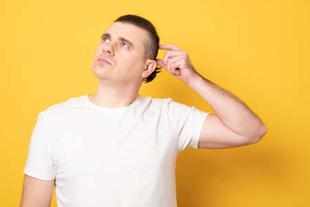 Young handsome man wearing casual t-shirt standing over yellow background confuse and wonder about question. Uncertain with doubt, thinking with hand on head. Pensive concept.の写真素材