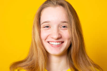 Close-up portrait of a cheerful girl. Studio portrait of a smiling teenage girl on a yellow background.の写真素材