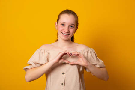 Be my valnetine. Charming young girl confesses in love, shows heart gesture, smiles broadly, has...