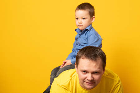 Portrait of emotional dad and his son on yellow backgroundの写真素材