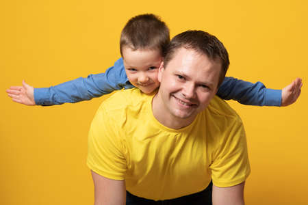 Portrait of emotional dad and his son on yellow backgroundの写真素材