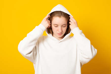 Beautiful teenage girl in a white hoodie cute smiling on yellow background.