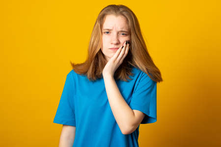 Beautiful caucasian woman with blonde hair wearing casual blue t-shirt touching mouth with hand with painful expression because of toothache or dental illness on teeth. Dentist.の写真素材