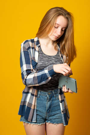 Teen girl holding wallet with dollar banknotes on yellow background. Money savings concept